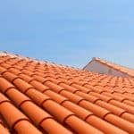 A wide view of a sunlit terracotta tile roof, showing rows of curved tiles leading toward a clear blue sky.