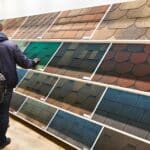 Two customers browse a showroom wall of roofing shingle sample panels of varying colors and shapes on display.